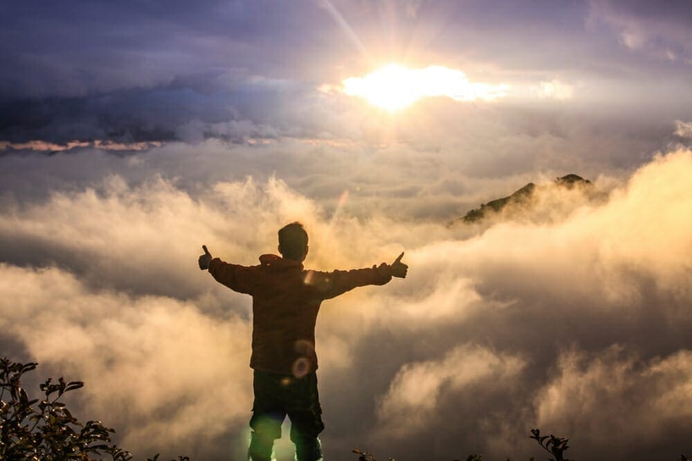 A man standing on top of a mountain with his arms outstretched A man standing on top of a mountain with his arms outstretched.