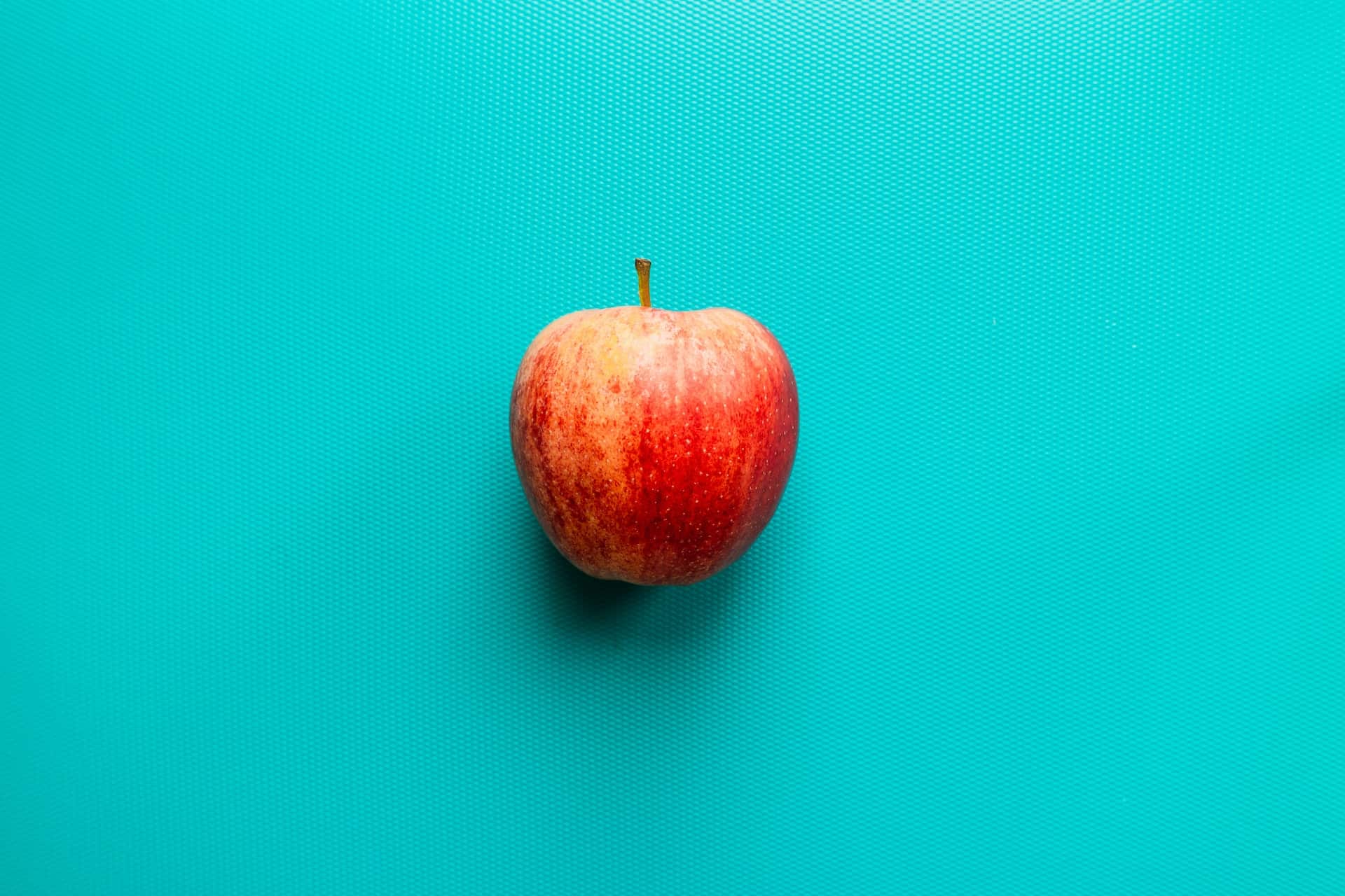 A red apple on a turquoise background A red apple on a turquoise background.