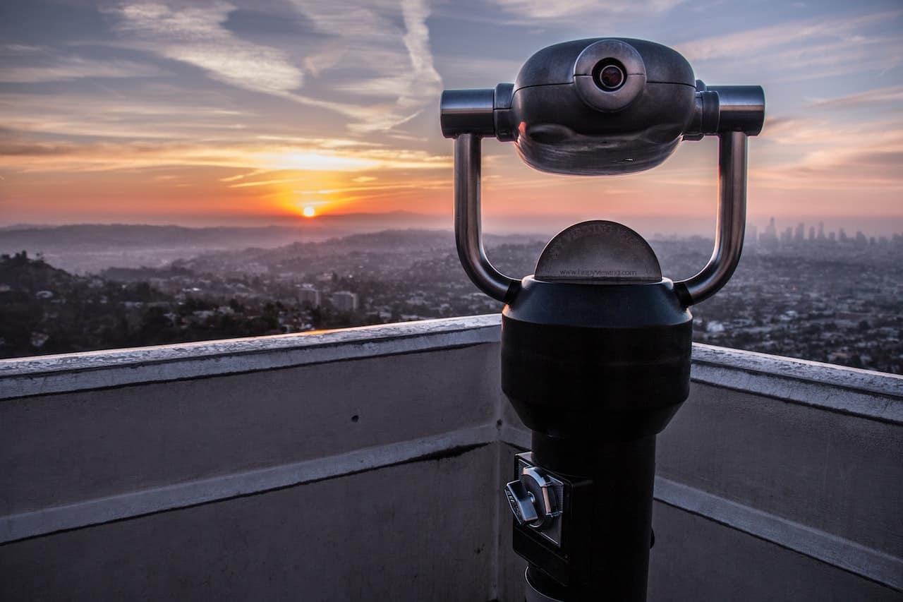 A binocular sits on top of a rooftop overlooking a city A binocular sits on top of a rooftop overlooking a city.